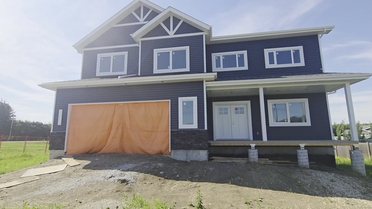 Dark-sided home with white window trim, gable accents and porch roofline while construction continues