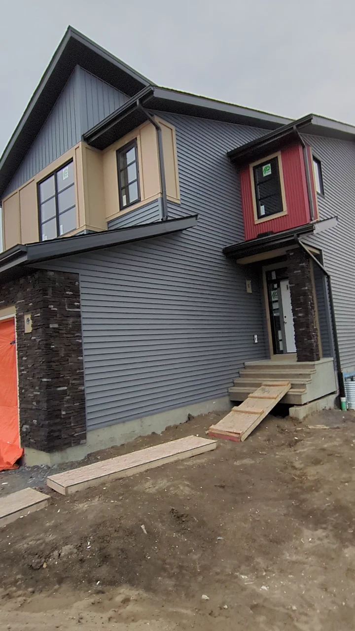 Grey siding with contrasting panels and dark roofline trim on a home under construction