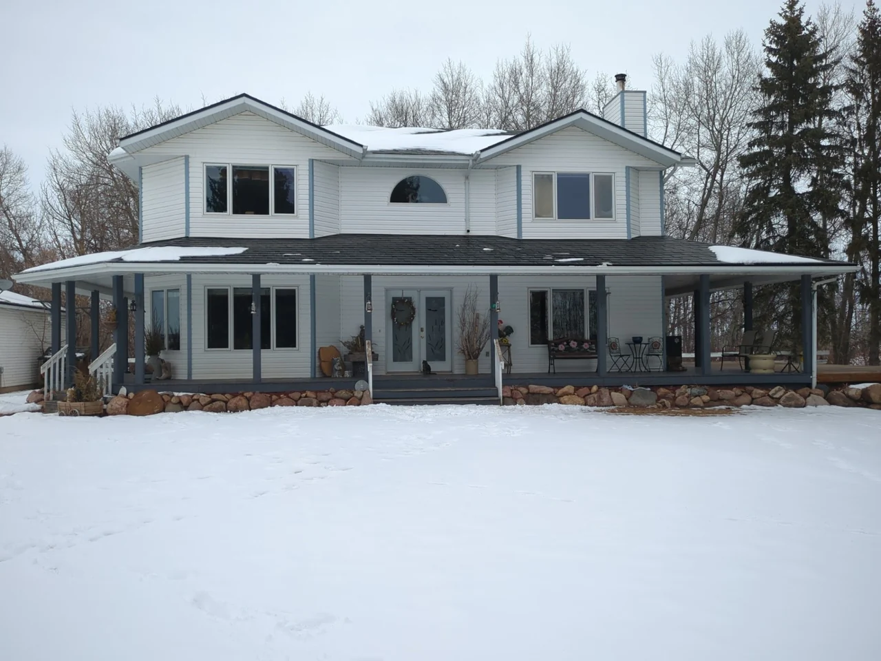 Original white siding and blue trim on a two-storey home with a wraparound porch before renovation