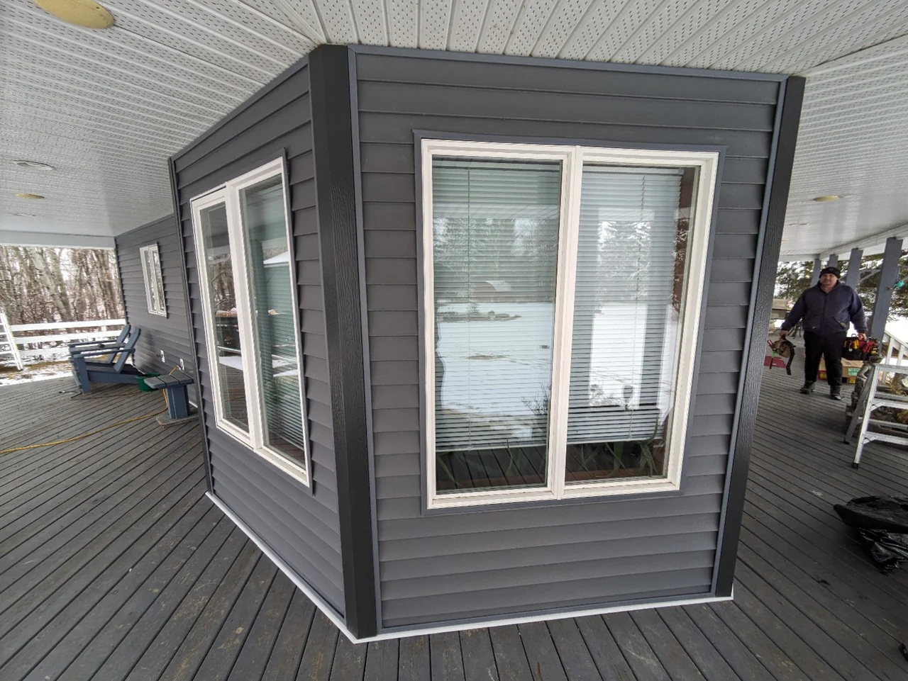 Vinyl siding and dark corner capping around windows beneath the wraparound porch