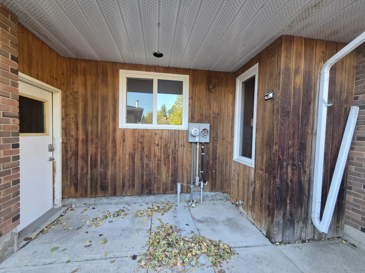 Weathered wood cladding around windows and utility meters before the vinyl renovation