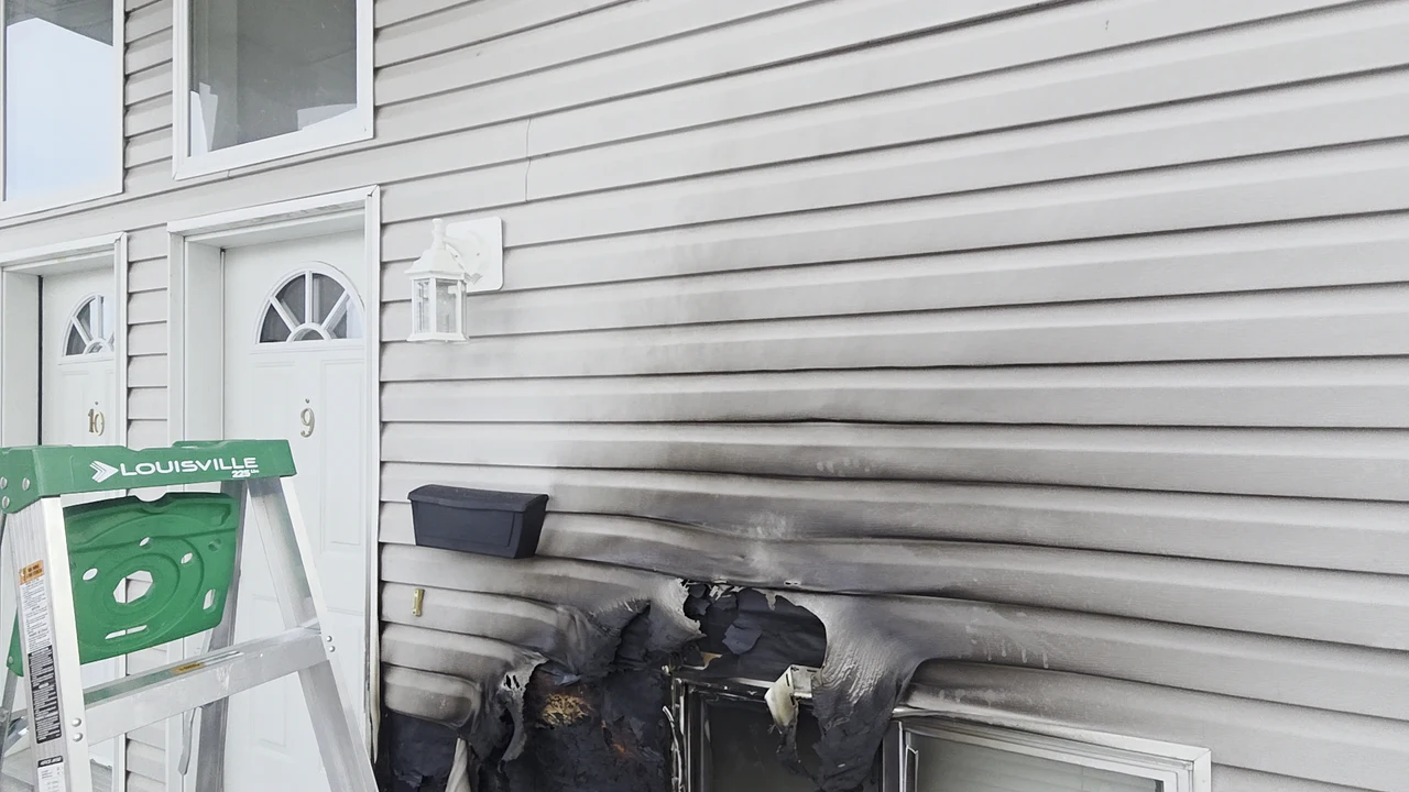 Scorched and distorted vinyl siding beside a basement window before repair